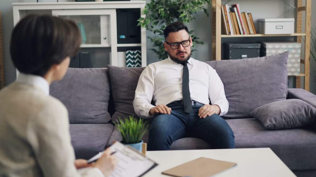 A man talking openly with a therapist during a supportive session under a sign for Ketamine Treatment for PTSD Trauma in Bloomington, Minnesota.